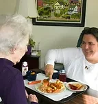 A Personal Care Assistant serving a meal to a companion