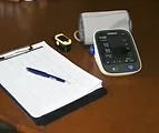 A blood pressure monitor beside a notepad and pen